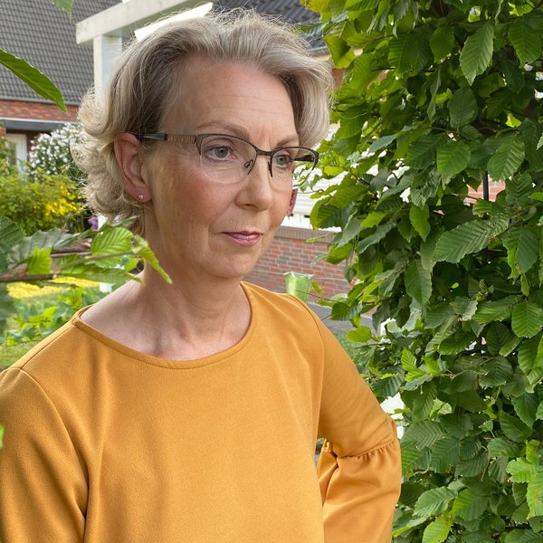Inhaberin Monika Ellinger-Hoffmann in ihrem Garten vor einer Buchenhecke.