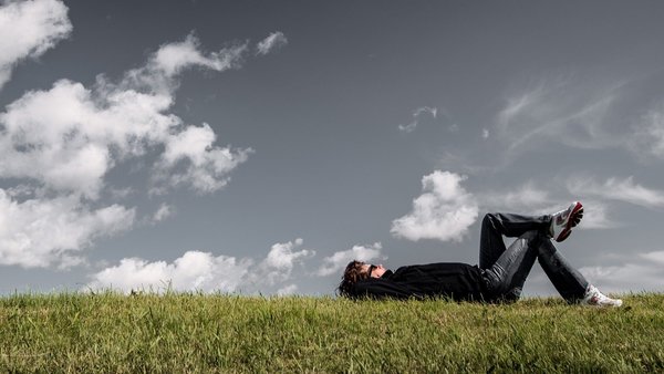 Ein Mann liegt entspannt auf einer Wiese und schaut in den Himmel.